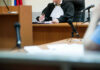 Judge at desk in courtroom with microphones visible