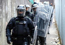 Police officers in riot gear down alleyway
