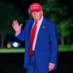 Trump Suggests New Holiday Honoring Charlie Kirk Man in suit wearing red hat outside at night