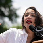 Person speaking passionately at outdoor event with microphones
