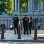Three police officers in dark uniforms standing outside building