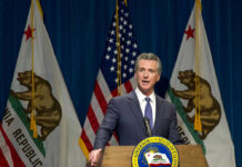 Newsom’s Top Aide INDICTED – Corruption Explodes in Sacramento Man speaking at podium with California and US flags