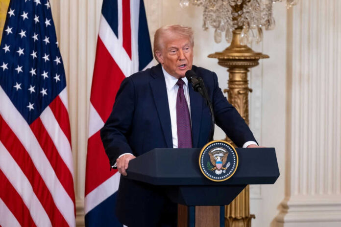 Man speaking at podium with USA and UK flags