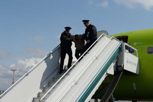 Police officers escorting a passenger down the stairs from an airplane