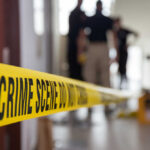 Yellow crime scene tape with blurred figures in the background